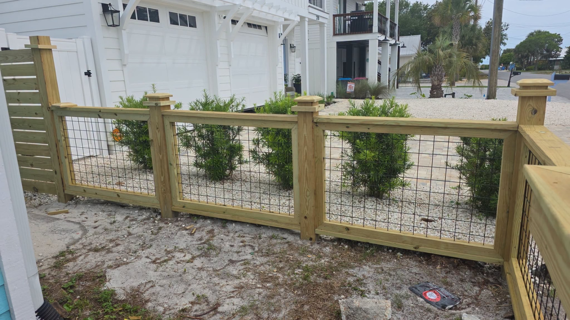 Framed wood and black wire-panel fence in front of a white coastal home
