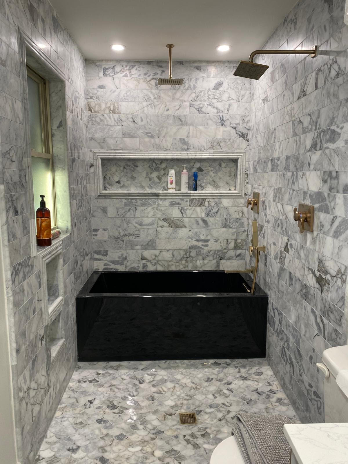Finished bathroom remodel with marble tile, black soaking tub and brass fixtures